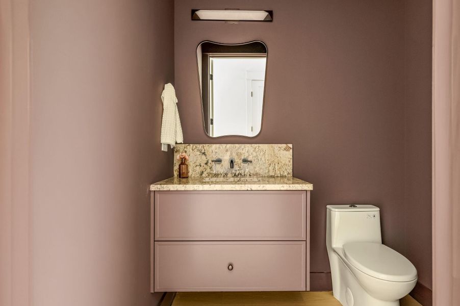 A well-appointed powder room features a floating vanity with a stone countertop and an artfully shaped mirror.