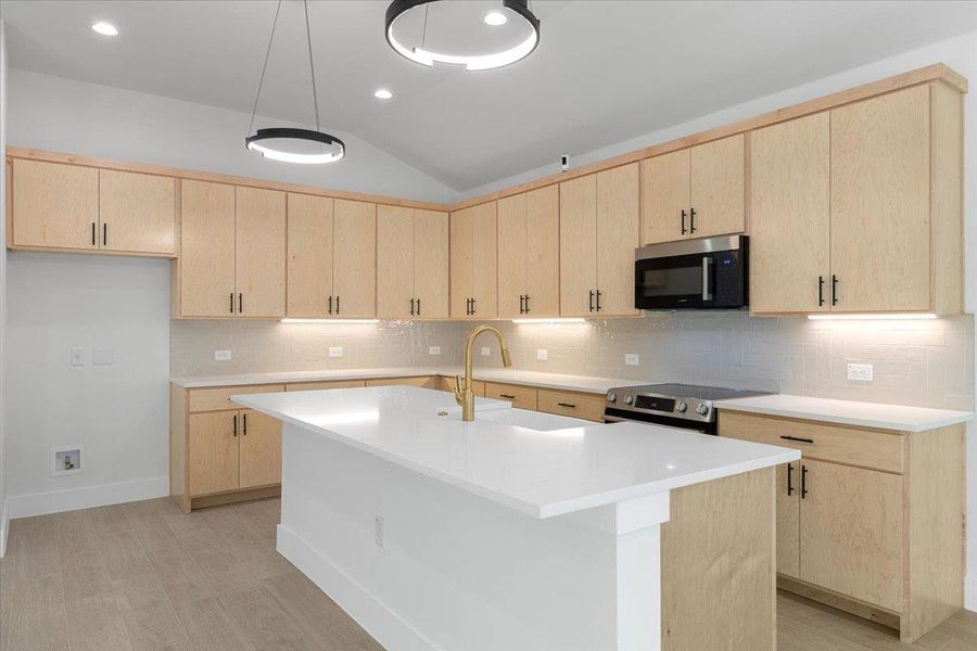 Kitchen featuring light brown cabinets, tasteful backsplash, vaulted ceiling, a center island with sink, and stainless steel appliances Kitchen featuring light brown cabinets, tasteful backsplash, vaulted ceiling, a center island with sink, and stainless steel appliances