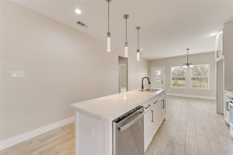 Kitchen with sink, dishwasher, an island with sink, pendant lighting, and white cabinets