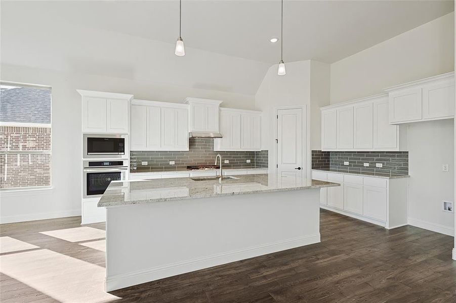 Kitchen featuring appliances with stainless steel finishes, decorative light fixtures, white cabinets, dark wood-type flooring, and a center island with sink