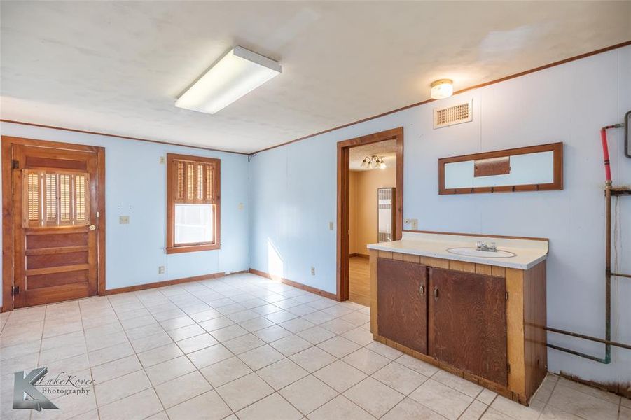 Kitchen with light countertops, brown cabinets, ornamental molding, and light tile patterned floors Kitchen with light countertops, brown cabinets, ornamental molding, and light tile patterned floors