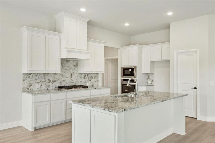 Contemporary kitchen featuring an island with a stainless steel sink, granite countertops, white cabinetry, a gas range, and a built-in microwave Contemporary kitchen featuring an island with a stainless steel sink, granite countertops, white cabinetry, a gas range, and a built-in microwave