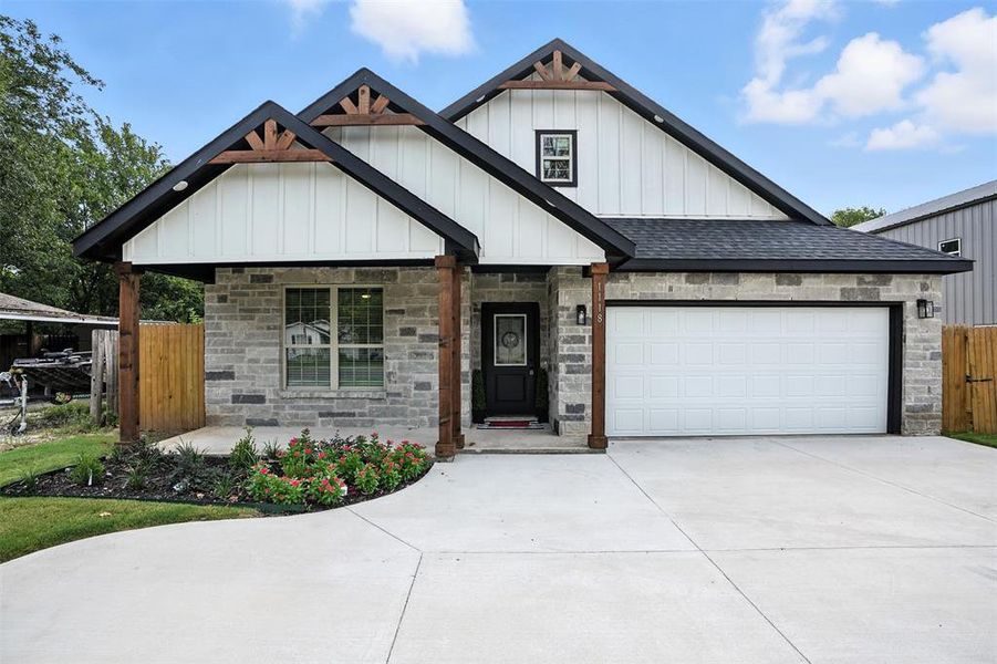 View of front of house featuring board and batten siding, roof with shingles, concrete driveway, stone siding, and covered porch