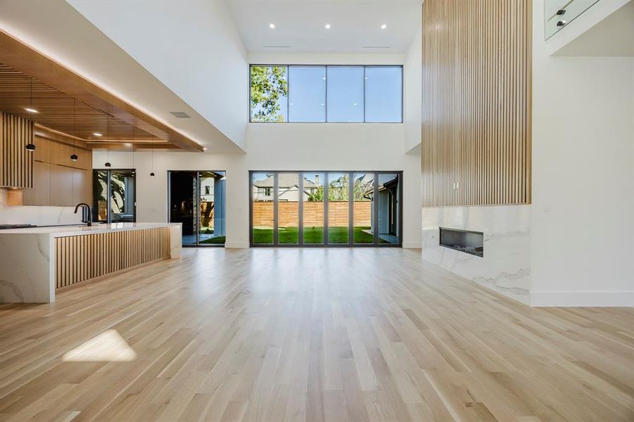 Unfurnished living room featuring light wood finished floors, recessed lighting, a premium fireplace, and a high ceiling Unfurnished living room featuring light wood finished floors, recessed lighting, a premium fireplace, and a high ceiling