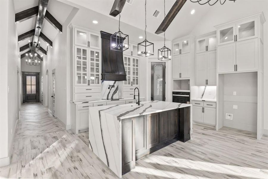 Kitchen featuring glass insert cabinets, white cabinets, light stone countertops, a kitchen island with sink, and pendant lighting Kitchen featuring glass insert cabinets, white cabinets, light stone countertops, a kitchen island with sink, and pendant lighting