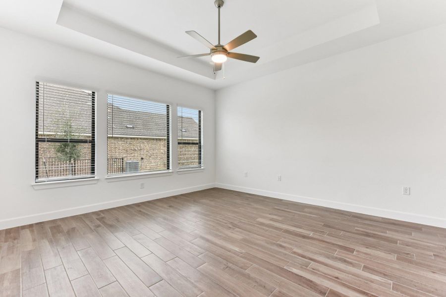 Empty room with a tray ceiling, light wood finished floors, and ceiling fan Empty room with a tray ceiling, light wood finished floors, and ceiling fan