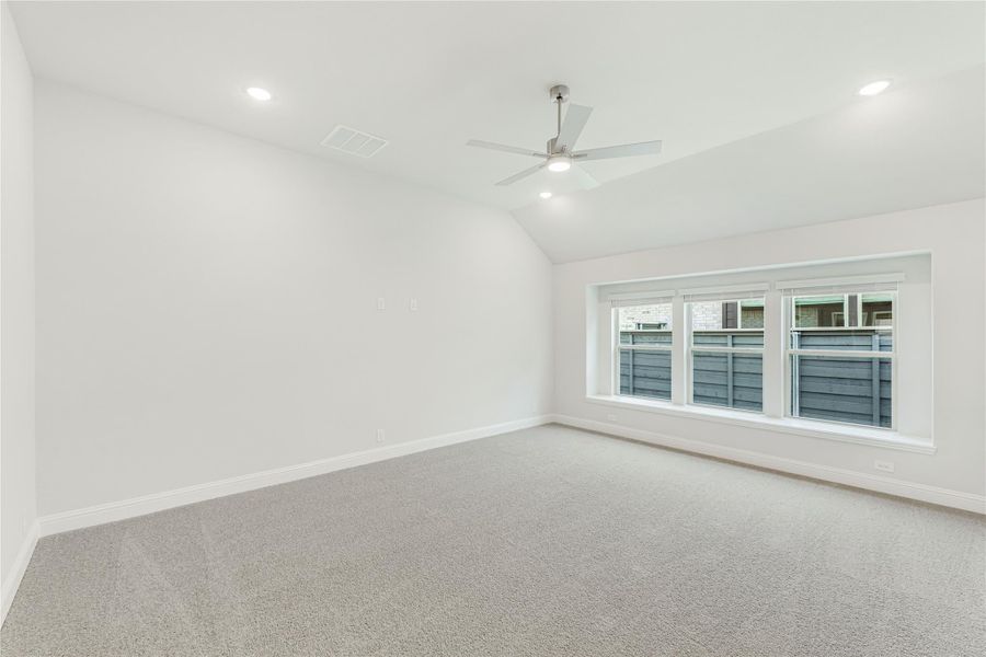 Empty bedroom with vaulted ceiling, ceiling fan, carpet flooring, and large window with exterior view Empty bedroom with vaulted ceiling, ceiling fan, carpet flooring, and large window with exterior view