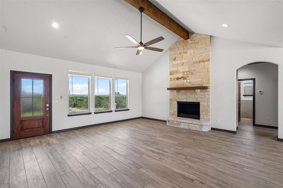 Unfurnished living room featuring ceiling fan, arched walkways, wood finished floors, beamed ceiling, and plenty of natural light