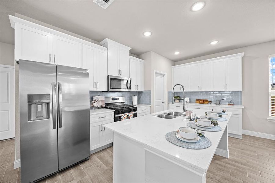 This stunning, light-filled kitchen is a chef's dream, featuring an abundance of crisp white cabinetry that extends to the ceiling for maximum storage. A beautiful, light-blue subway tile backsplash adds a soft pop of color, perfectly complementing the beautiful countertops and the black and stainless steel appliances, which include a gas range and a built-in microwave.