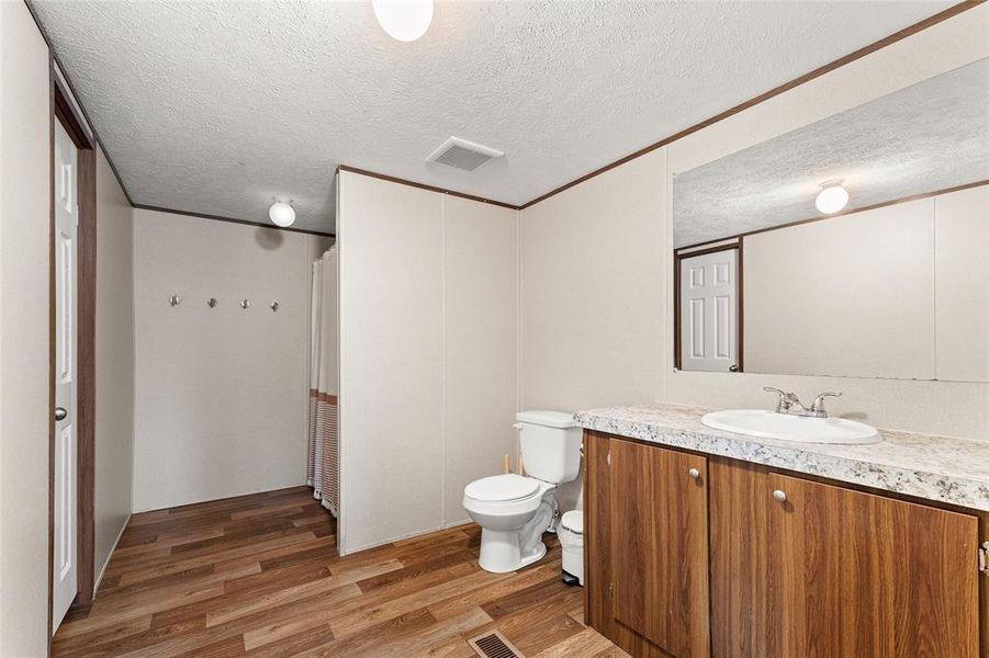 Bathroom with curtained shower, vanity, light wood-style floors, and a textured ceiling