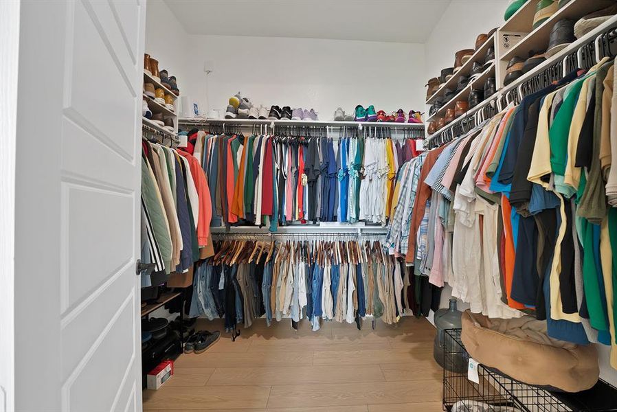 Spacious walk-in closet featuring extensive built-in shelving, multiple hanging rods, and light wood-finish flooring Spacious walk-in closet featuring extensive built-in shelving, multiple hanging rods, and light wood-finish flooring