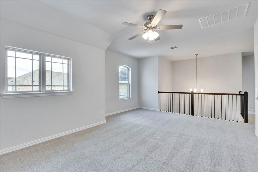 Carpeted empty room featuring healthy amount of natural light, a ceiling fan, and a chandelier Carpeted empty room featuring healthy amount of natural light, a ceiling fan, and a chandelier