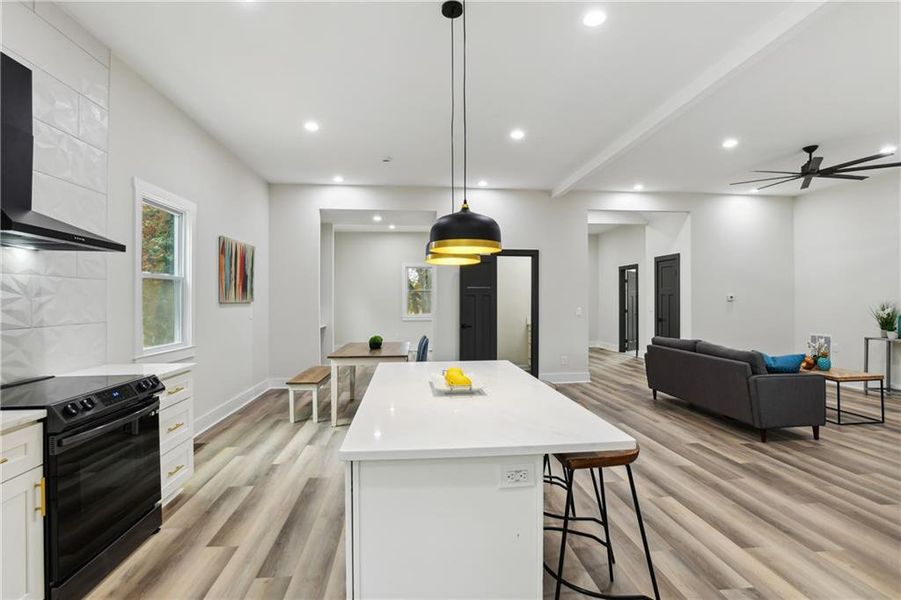 Kitchen with a center island, black range with electric cooktop, pendant lighting, wall chimney exhaust hood, and white cabinetry