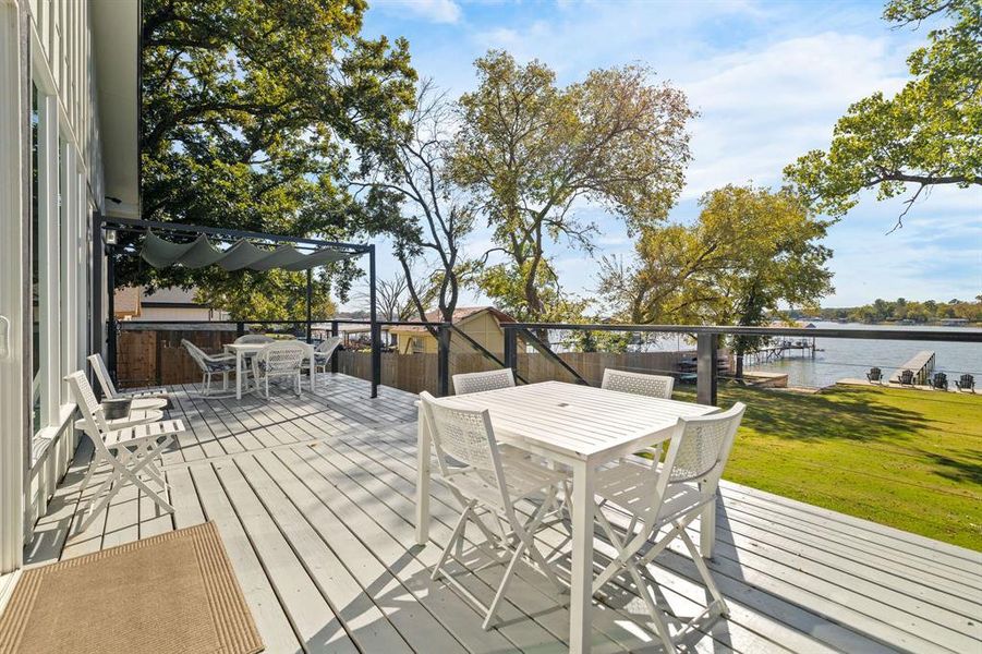 Deck with a water view, outdoor dining space, and a lawn