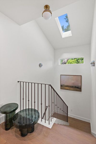 A skylight and high windows illuminate this well-designed staircase with hardwood flooring and sleek railings.