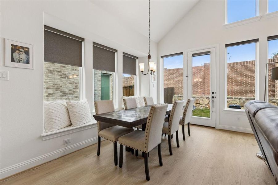 Bright dining space featuring vaulted ceilings, a built-in window seat, large windows with roller shades, a glass-paned door, and wood-finish flooring