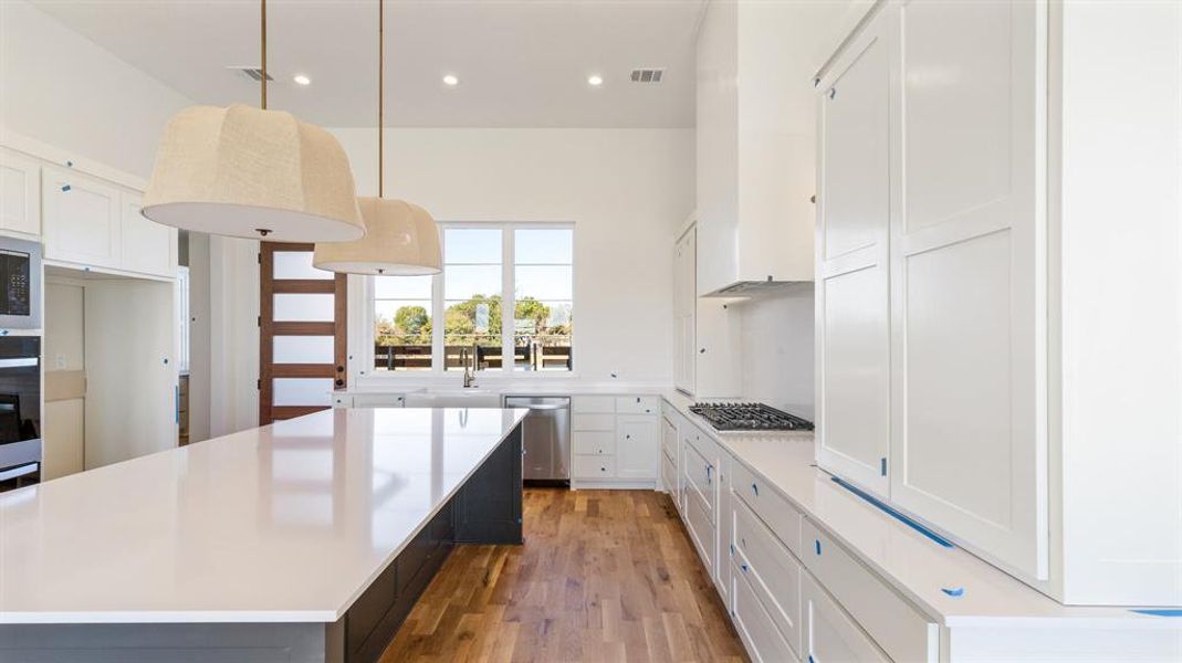 Kitchen featuring appliances with stainless steel finishes, pendant lighting, wood-type flooring, a center island, and white cabinetry