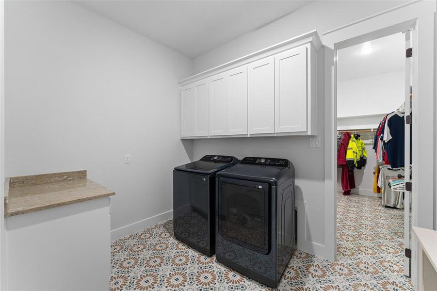 Laundry area featuring patterned tile flooring, a granite-finish countertop, and white shaker-style cabinetry