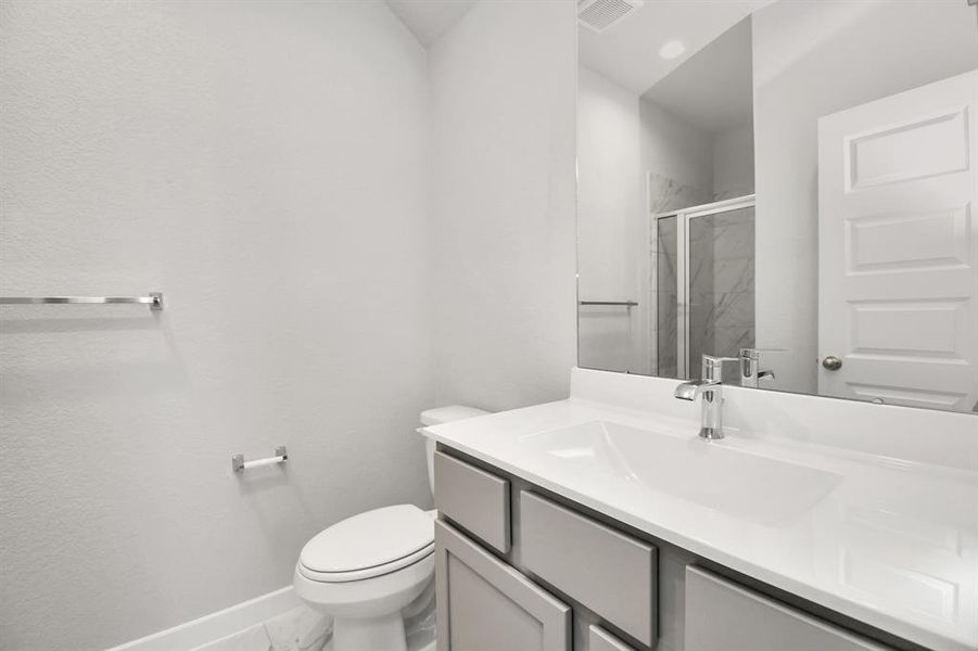 Experience sophistication in the guest suite bathroom, where tile flooring complements a walk-in shower with tile surround. Light wood cabinets complete with a beautiful light countertop, enhances the space for a truly inviting ambiance. Sample photo of completed home with similar floor plan. Actual colors and selections may vary.