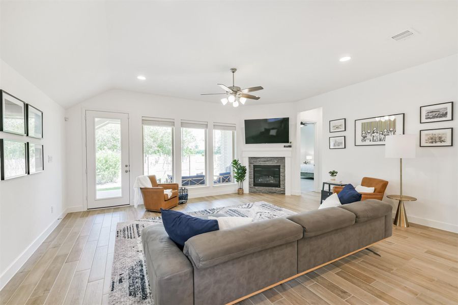 A corner gaslog fireplace and wall of windows anchor this large living room with high ceilings, a fan, and views to the private backyard. A corner gaslog fireplace and wall of windows anchor this large living room with high ceilings, a fan, and views to the private backyard.