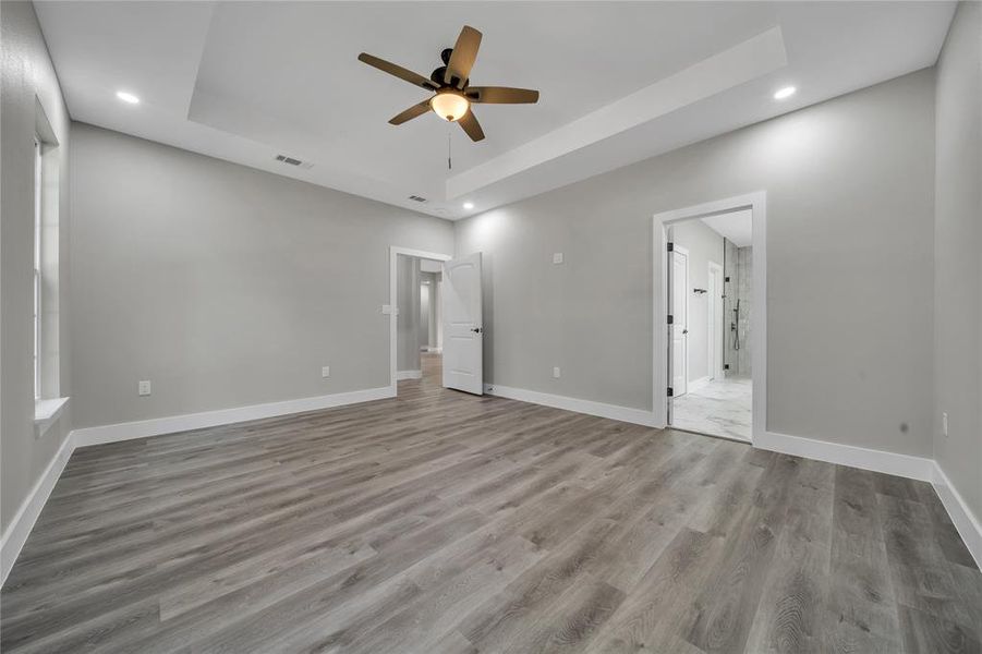 Unfurnished bedroom with wood-type flooring, ceiling fan, and a tray ceiling