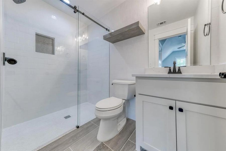 Bathroom featuring toilet, vanity, an enclosed shower, and tile walls