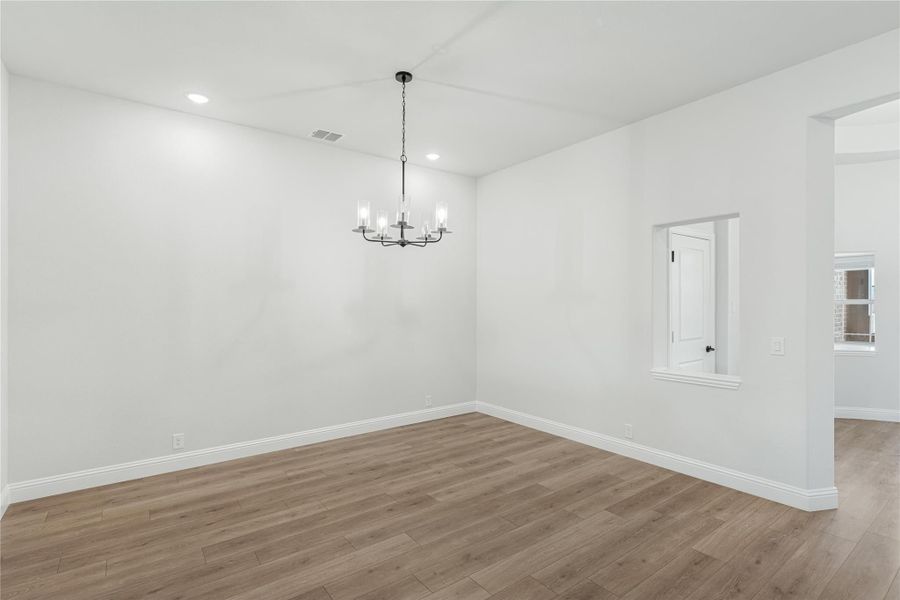 Empty dining room with wood-look floors, white walls, and a black chandelier with glass shades