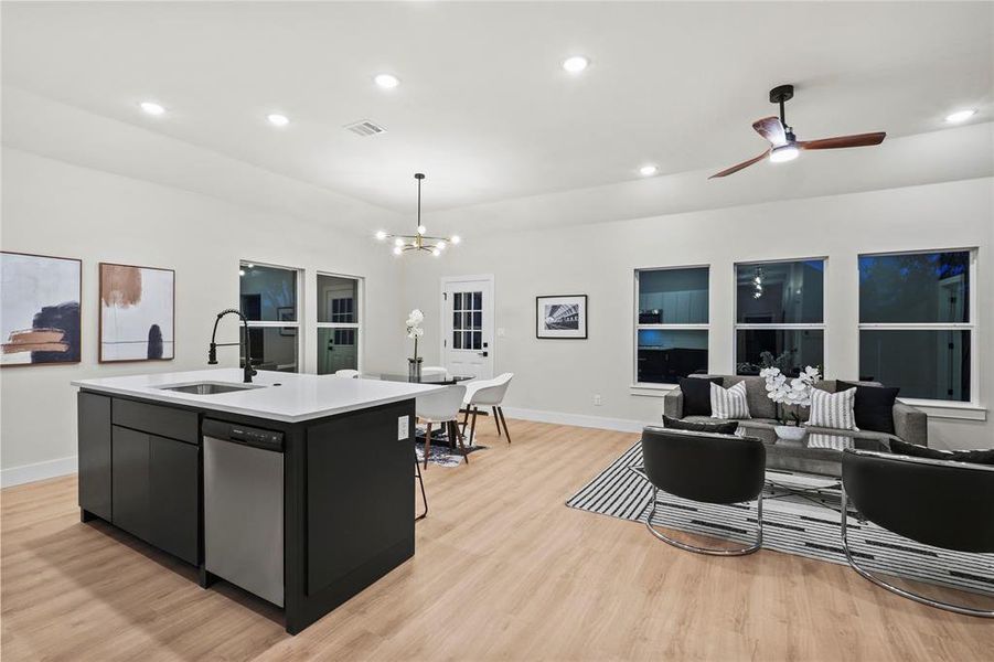 Kitchen with light wood-type flooring, sink, a center island with sink, dishwasher, and hanging light fixtures