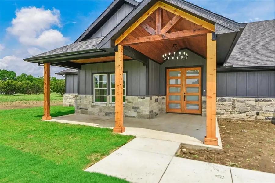 View of exterior entry with board and batten siding, roof with shingles, stone siding, and covered porch View of exterior entry with board and batten siding, roof with shingles, stone siding, and covered porch