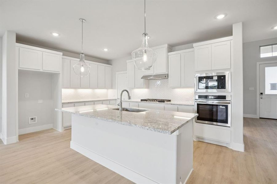 Kitchen with stainless steel appliances, backsplash, white cabinetry, hanging light fixtures, and light wood-type flooring