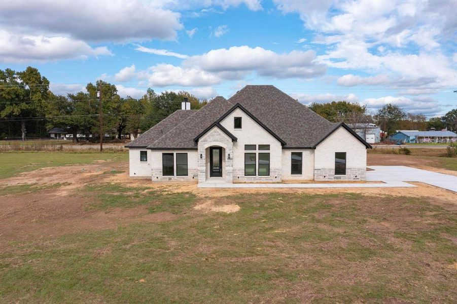 French provincial home featuring stone siding, a front yard, roof with shingles, and a chimney