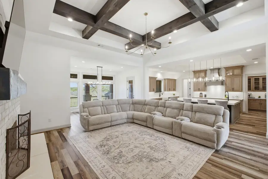 The living area features a white brick fireplace, wood-look flooring, and a coffered ceiling with exposed wood beams and a chandelier