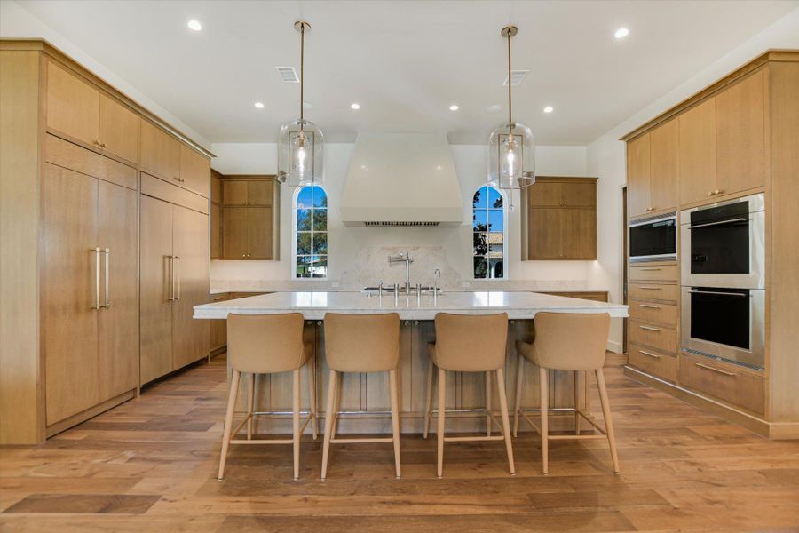 Kitchen featuring a breakfast bar area, a spacious island, light wood finished floors, and stainless steel double oven
