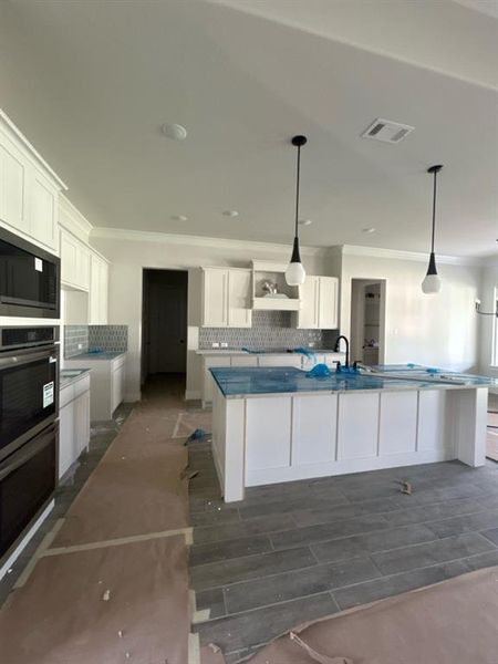 Modern kitchen featuring a large central island, white shaker cabinetry, stainless steel built-in appliances, decorative tile backsplash, and two pendant light fixtures Modern kitchen featuring a large central island, white shaker cabinetry, stainless steel built-in appliances, decorative tile backsplash, and two pendant light fixtures
