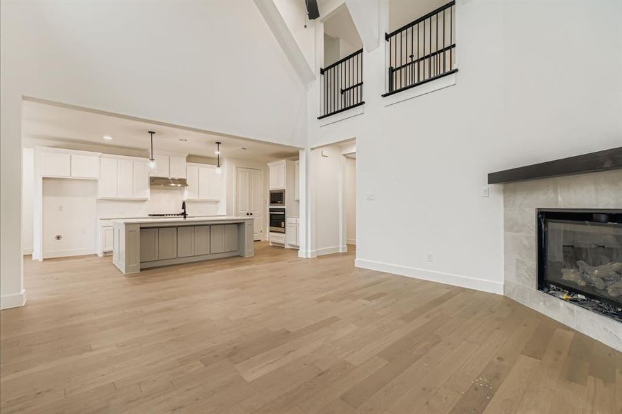 Unfurnished living room with a fireplace, light wood finished floors, and a towering ceiling Unfurnished living room with a fireplace, light wood finished floors, and a towering ceiling