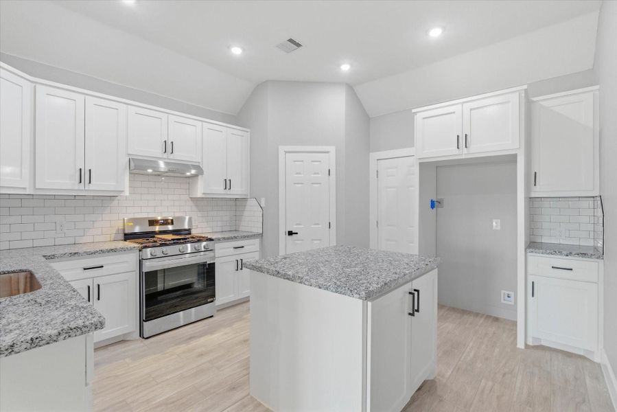 Sophisticated kitchen space features pristine white shaker cabinetry, elegant granite countertops, and a classic subway tile backsplash, as well as a functional island.