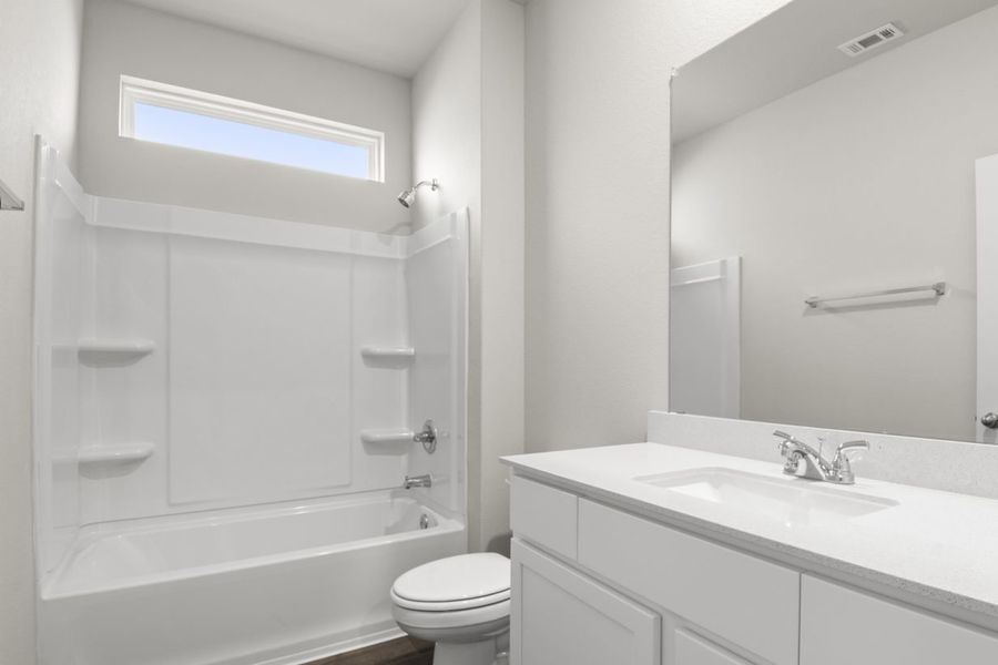 Image of a bathroom with light grey walls, white cabinets and vanity, a white shower and tub, and a window above the shower