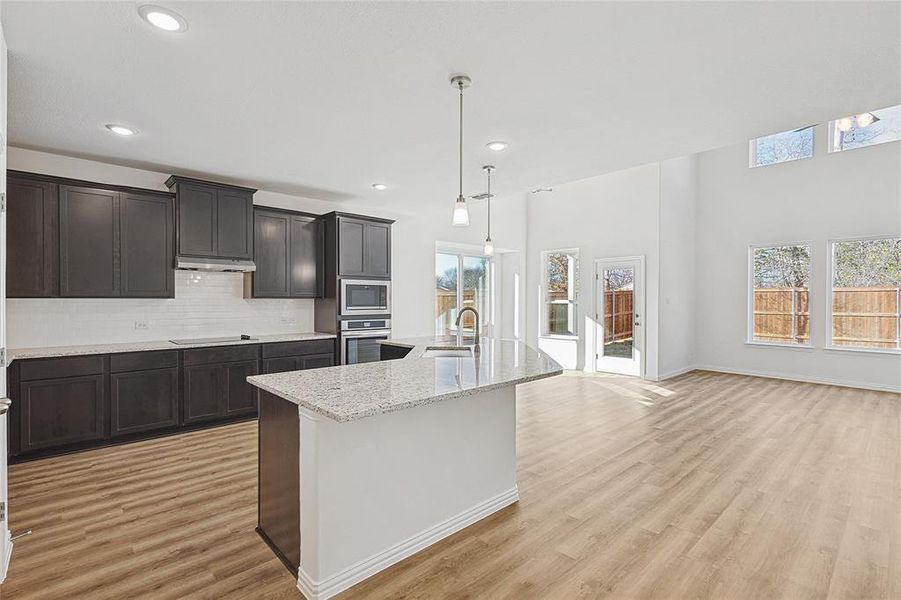 Kitchen featuring decorative backsplash, appliances with stainless steel finishes, light hardwood / wood-style flooring, hanging light fixtures, and an island with sink