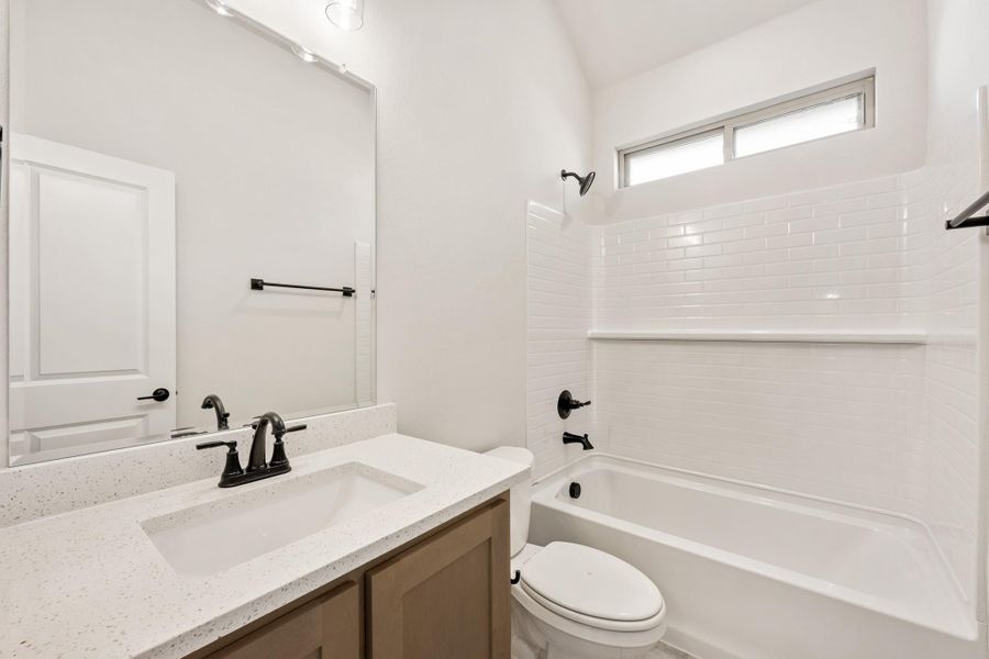 Full bathroom with quartz vanity, white subway tile tub surround, and black fixtures