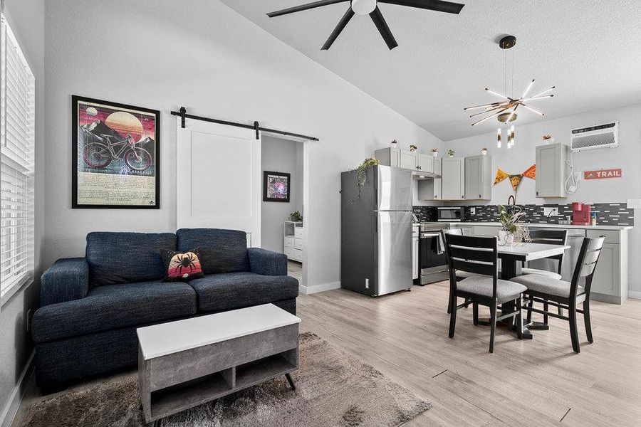 Living area with a barn door, light wood finished floors, high vaulted ceiling, a ceiling fan, and a chandelier.