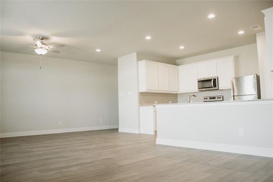 Kitchen featuring tasteful backsplash, white cabinets, light wood-type flooring, and appliances with stainless steel finishes