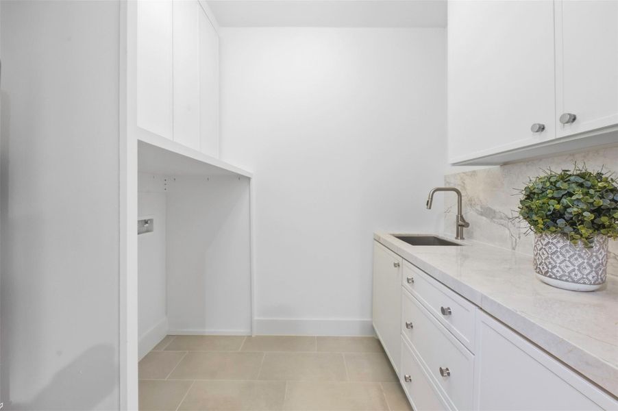 Large walk-in laundry room features a utility sink, generous counter space, and extensive built-in storage for linens, cleaning supplies, brooms, vacuums, Roombas, and more.