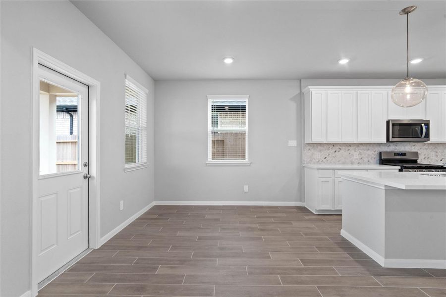 Enjoy meals in this sun-drenched space, featuring durable luxury vinyl flooring, abundant natural light from the large windows (fitted with blinds), and recessed lighting. An access door to the back covered patio is conveniently located for ease of indoor to outdoor living.