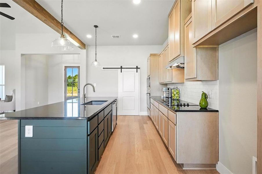 Kitchen with a barn door, a center island with sink, light wood finish cabinets, light wood-type flooring, and beam ceiling