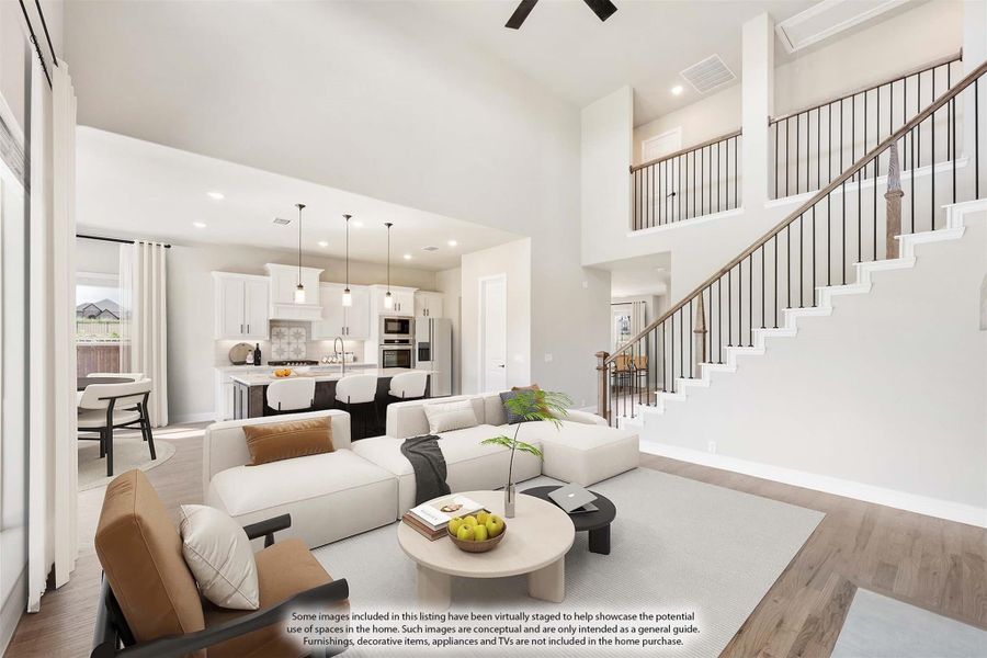 Open-concept living room with two-story ceiling, staircase, and kitchen visible in background