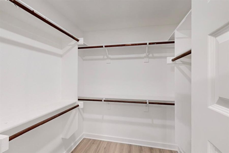 Walk in closet with light hardwood / wood-style floors