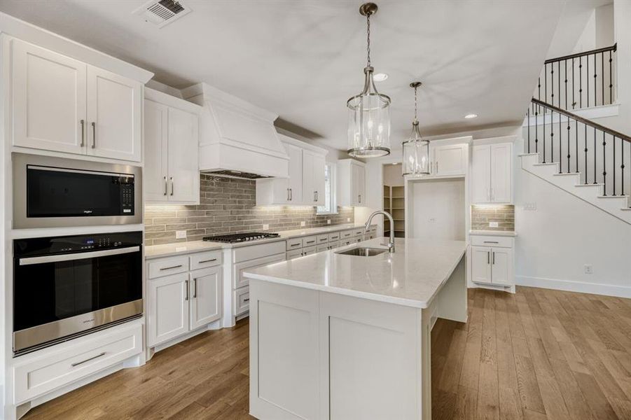 Kitchen with stainless steel appliances, white cabinets, hanging light fixtures, light wood-style flooring, and an island with sink