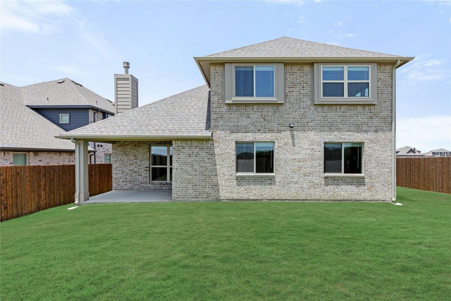Two-story brick home rear view with covered patio, large green backyard, and wood privacy fence