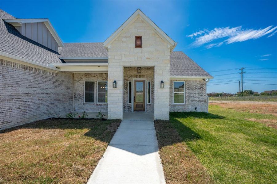 Doorway to property with roof with shingles, a yard, brick siding, and board and batten siding Doorway to property with roof with shingles, a yard, brick siding, and board and batten siding