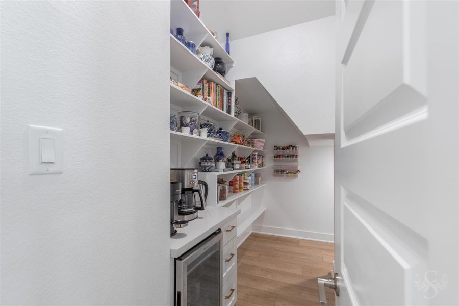 Exceptional walk-in pantry offers an impressive amount of open shelving for organized storage. A quartz counter with cabinetry creates a dedicated space for a mini fridge (stays with home) and beverage preparation. Exceptional walk-in pantry offers an impressive amount of open shelving for organized storage. A quartz counter with cabinetry creates a dedicated space for a mini fridge (stays with home) and beverage preparation.